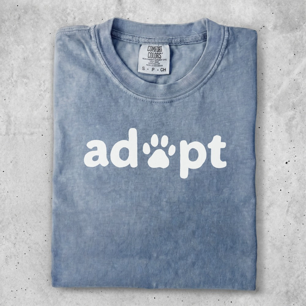 Blue t-shirt with white "adopt" text and paw print graphic.