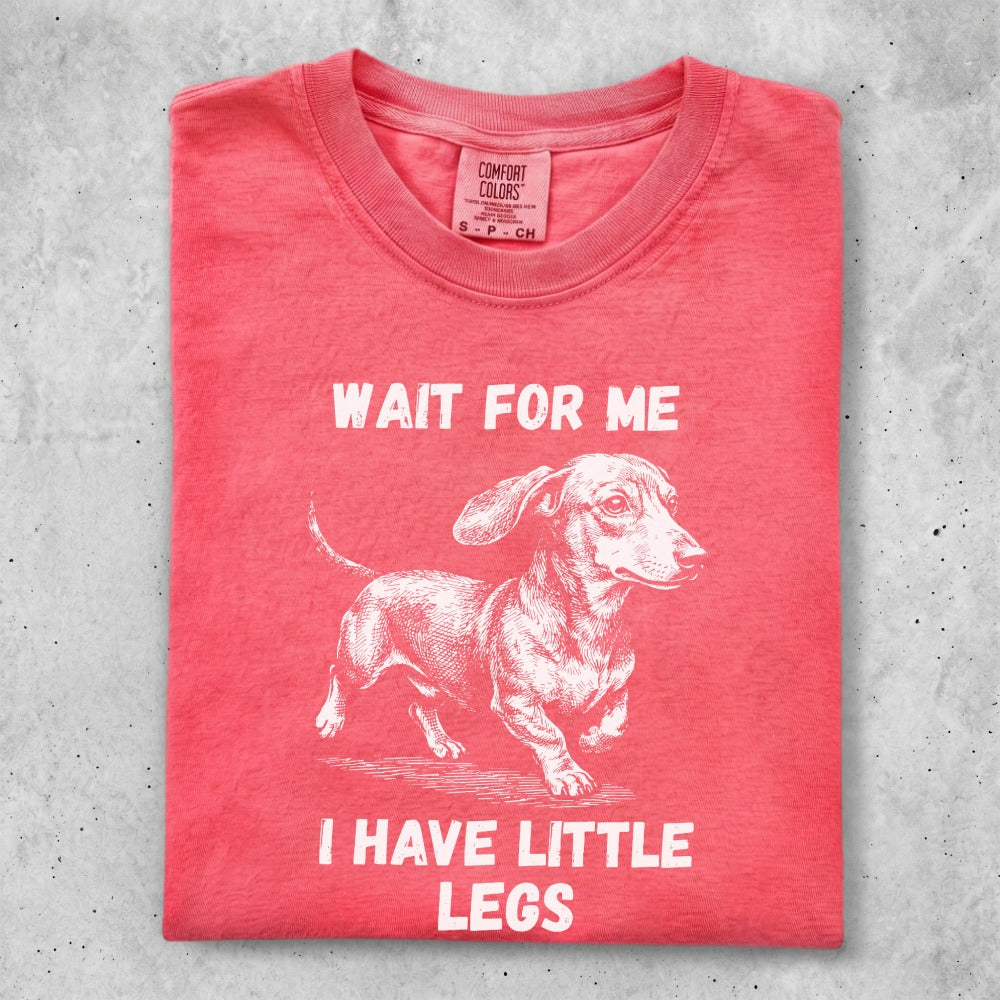Coral Comfort Colors t-shirt with "WAIT FOR ME I HAVE LITTLE LEGS" and dachshund graphic.
