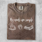 Brown t-shirt with "My needs are simple" text, coffee cup, paw print, and books.