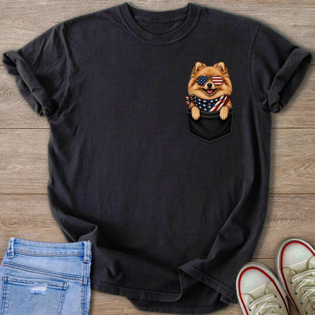 Pomeranian dog wearing American flag bandana and sunglasses peeking from t-shirt pocket.