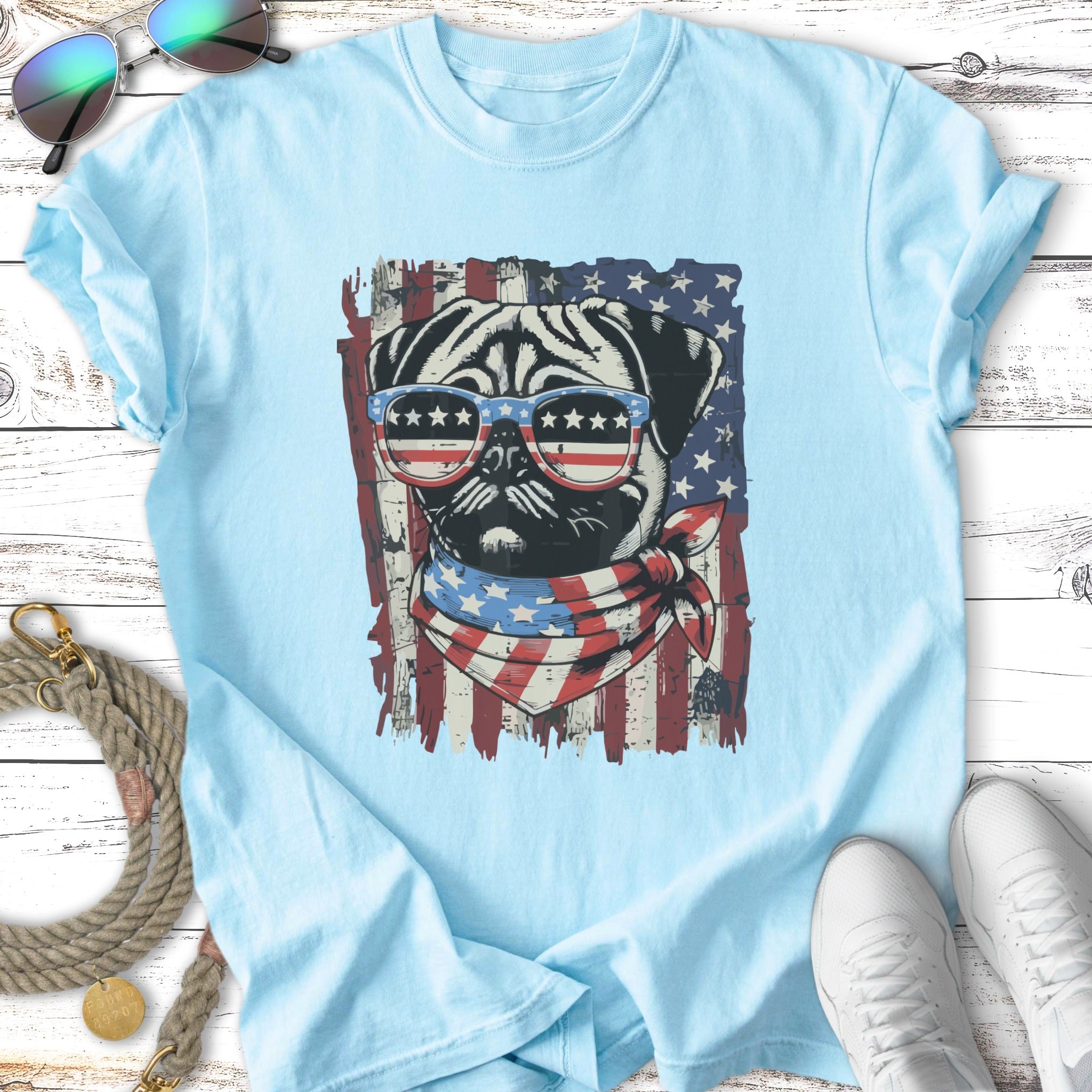 Pug wearing sunglasses and bandana with American flag design on t-shirt.