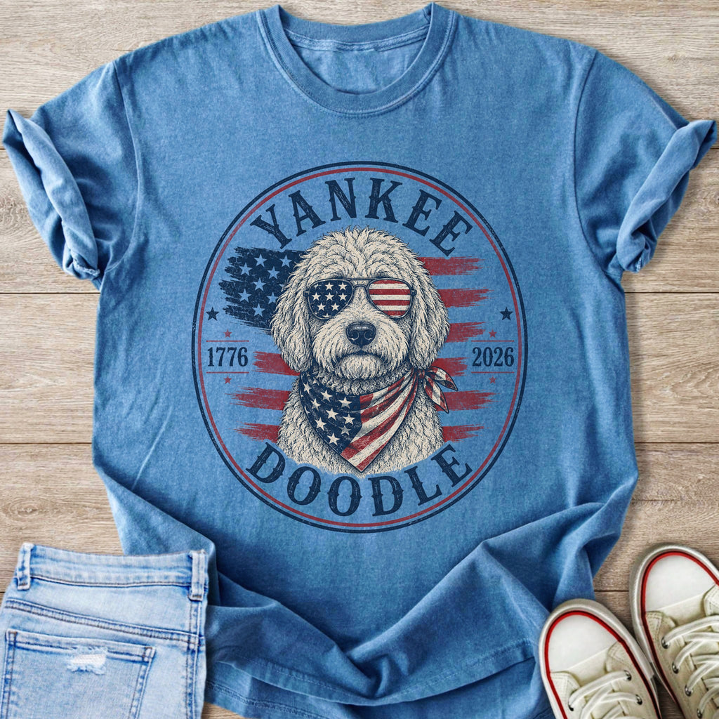 Blue t-shirt with a doodle wearing American flag sunglasses and bandana, "Yankee Doodle 1776 2026".