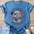 Blue t-shirt with a doodle wearing American flag sunglasses and bandana, "Yankee Doodle 1776 2026".