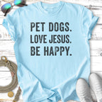 Light blue t-shirt with "PET DOGS. LOVE JESUS. BE HAPPY." in black text.