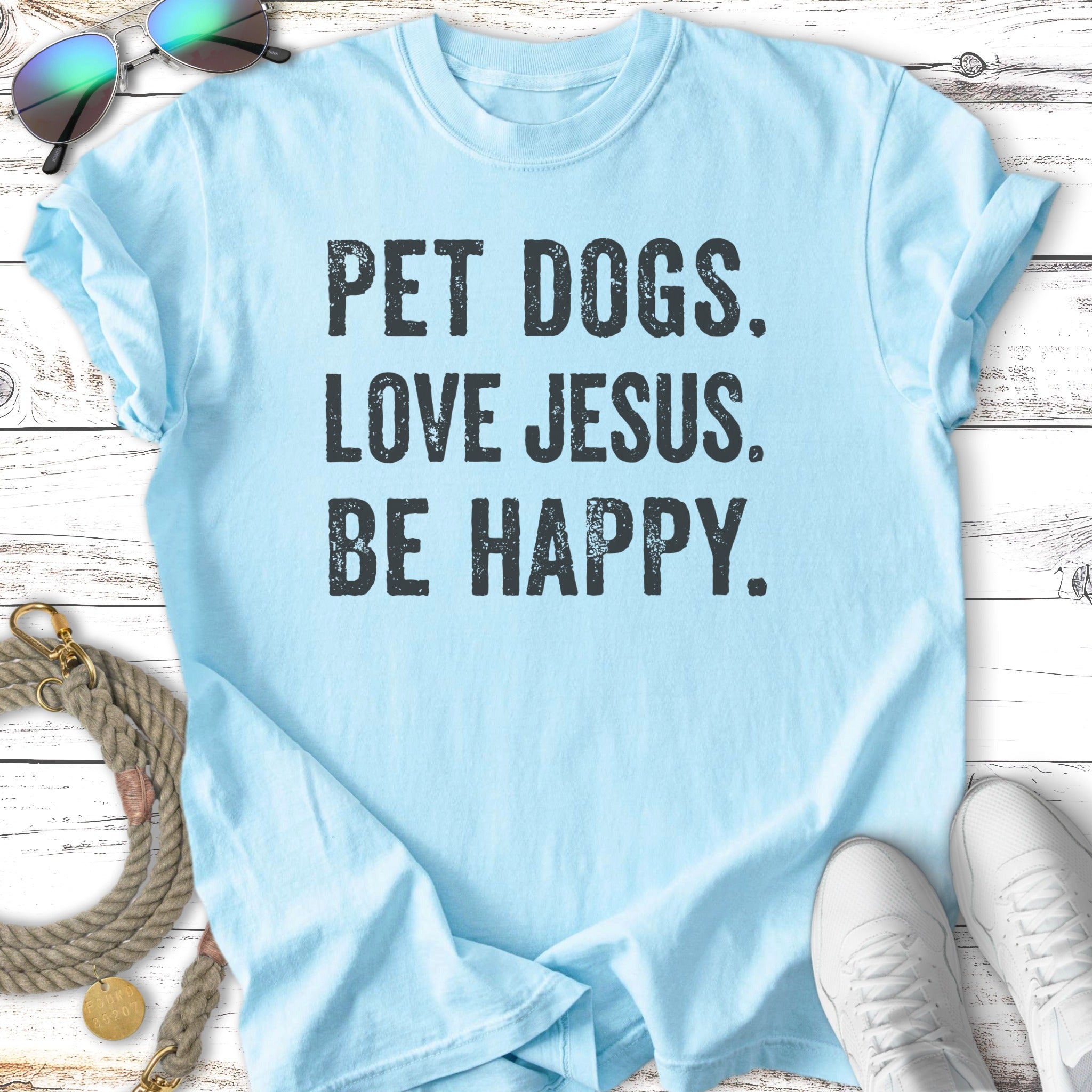 Light blue t-shirt with "PET DOGS. LOVE JESUS. BE HAPPY." in black text.