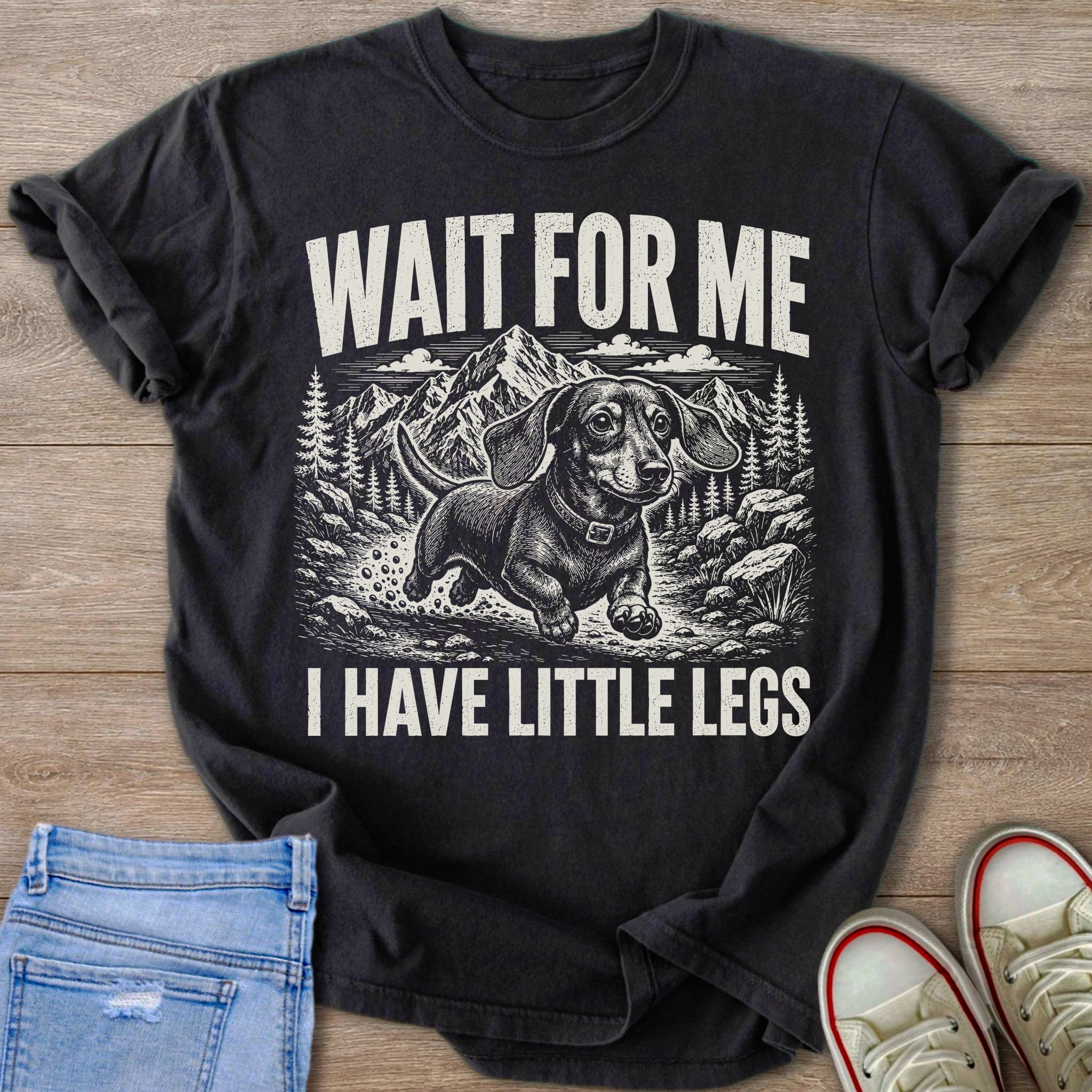 Black t-shirt with a black and white print of a dachshund running with mountains and "WAIT FOR ME I HAVE LITTLE LEGS"
