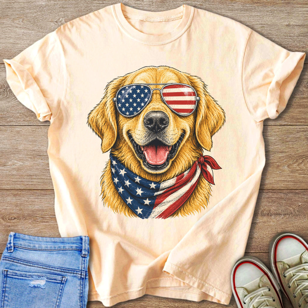 Golden retriever wearing American flag sunglasses and bandana on light peach t-shirt.