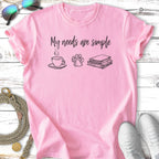 Pink t-shirt with "My needs are simple" and icons of coffee, paw print, and books.