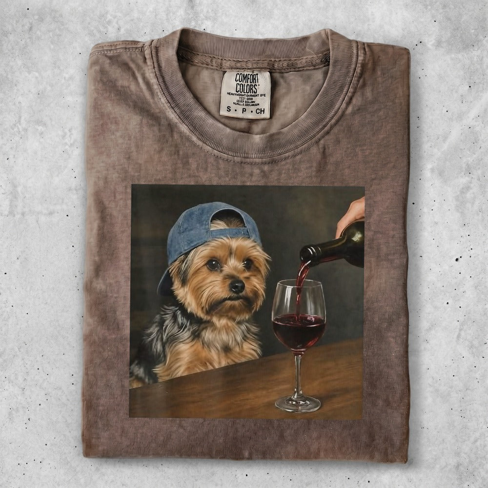 Yorkshire terrier wearing a baseball cap, being poured red wine into a glass.