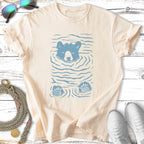 Blue bear emerging from water with paw prints on a cream t-shirt.