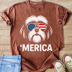 White dog wearing American flag sunglasses with 'MERICA text on shirt.