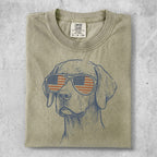 Line art of a dog wearing American flag sunglasses on a tan t-shirt.
