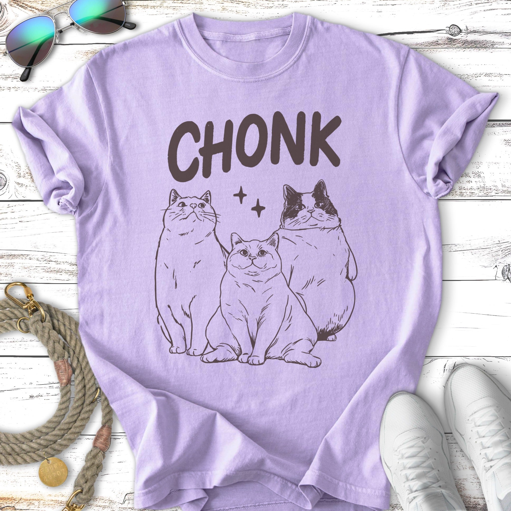 Three cats with text "CHONK" above them on a purple t-shirt.