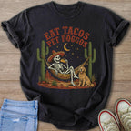 Skeleton in hammock with taco and dog, surrounded by cacti; text reads "Eat Tacos Pet Doggos".