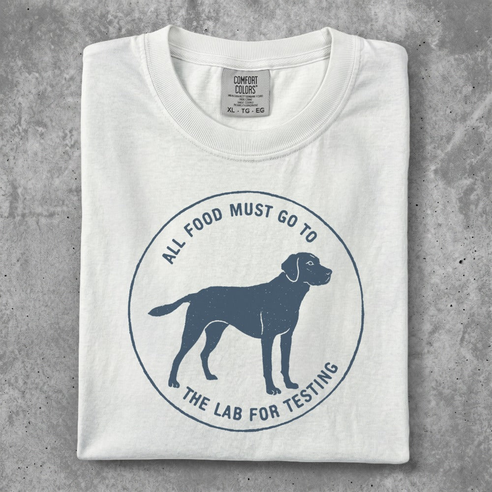 White t-shirt with a blue circular graphic of a dog and text "ALL FOOD MUST GO TO THE LAB FOR TESTING".