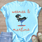 Light blue t-shirt with text "weenies & martinis" and a dachshund in a martini glass.