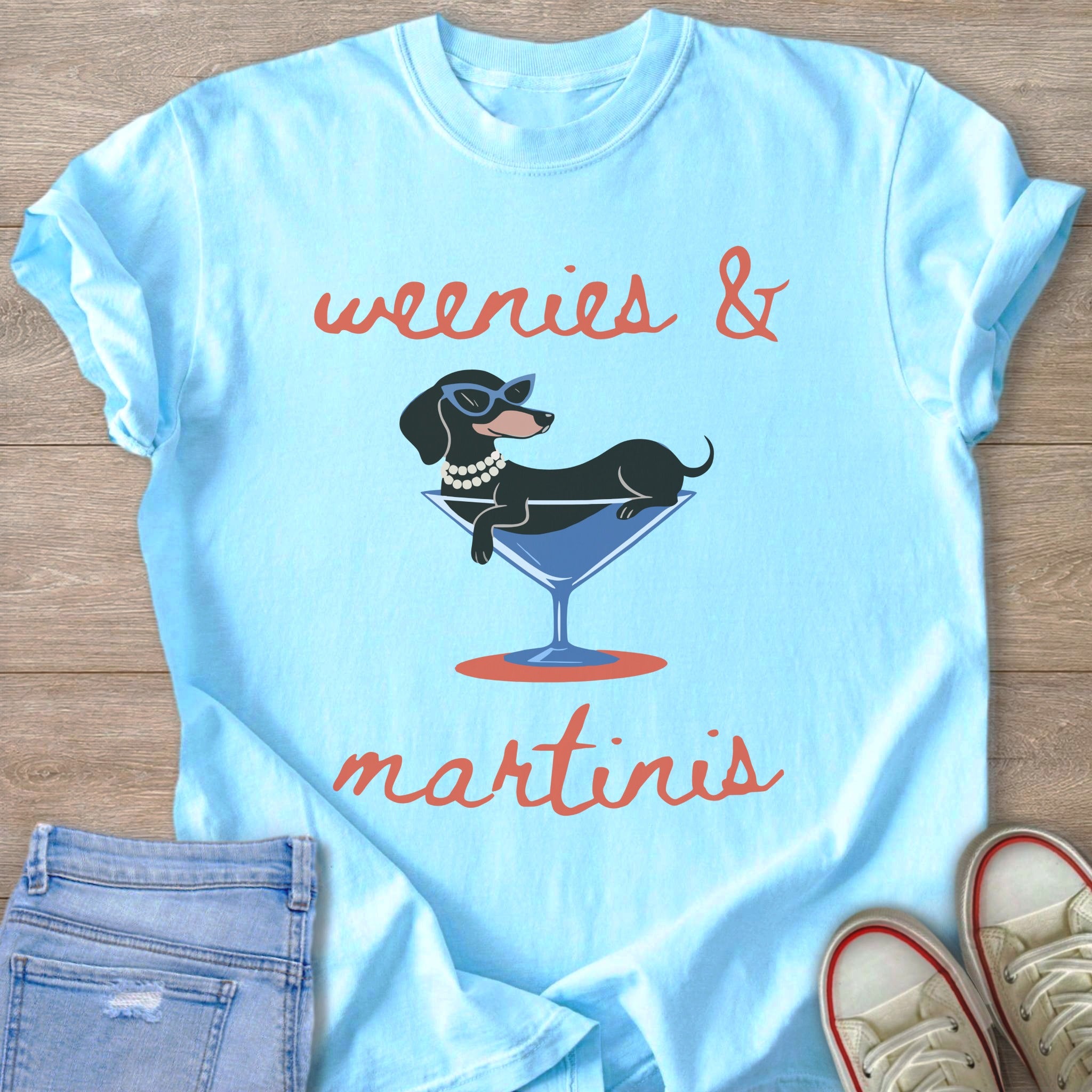 Light blue t-shirt with text "weenies & martinis" and a dachshund in a martini glass.