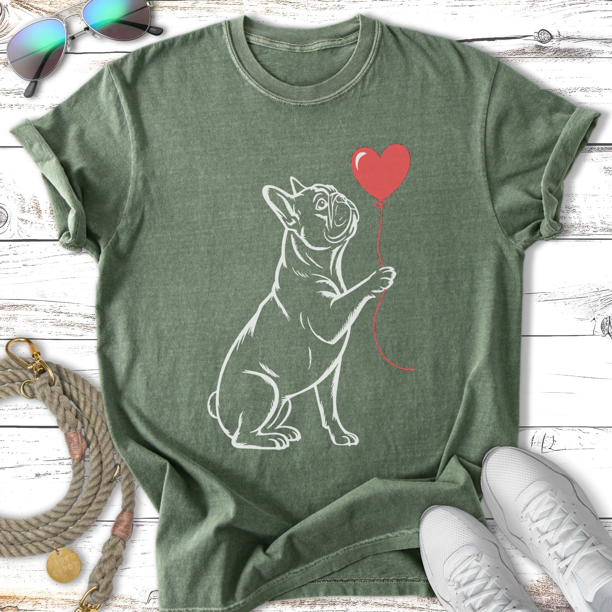 French bulldog holding a red heart balloon, outline sketch on a green t-shirt.