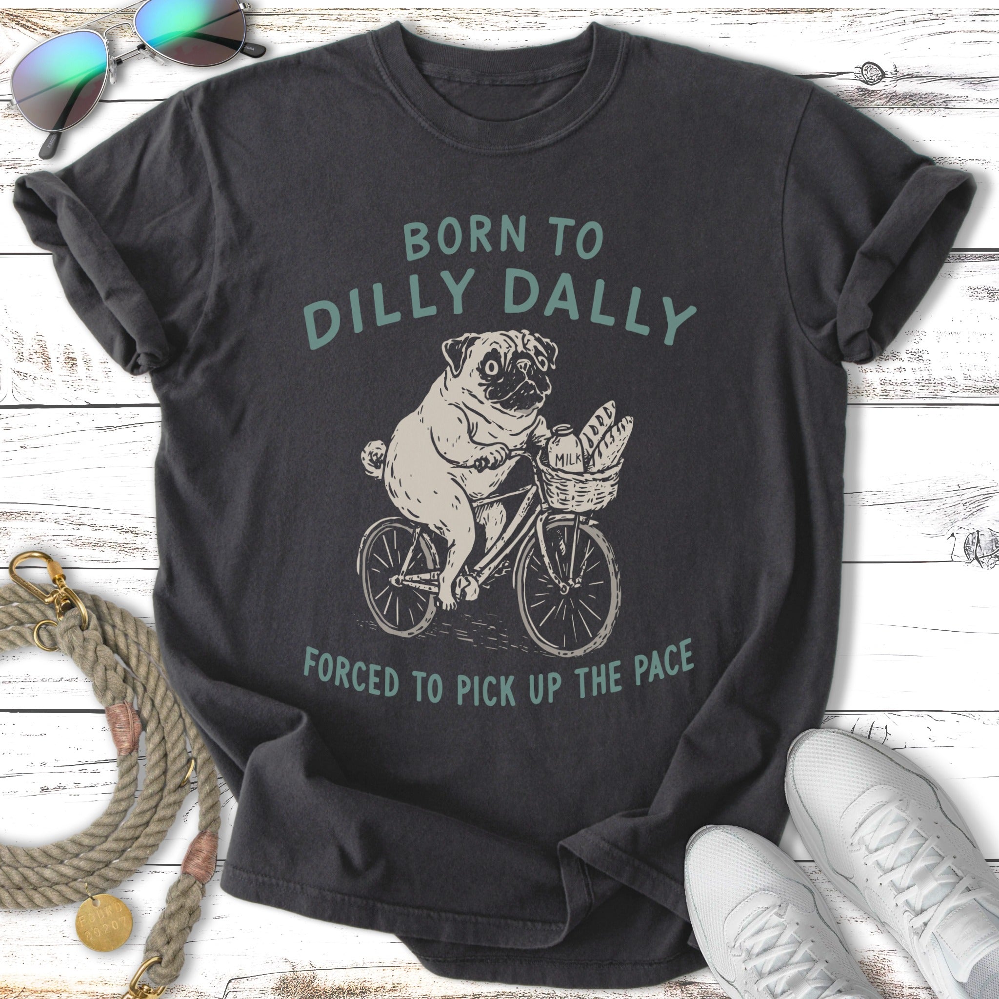 Dark t-shirt with pug on bicycle graphic and "Born to dilly dally forced to pick up the pace" text.