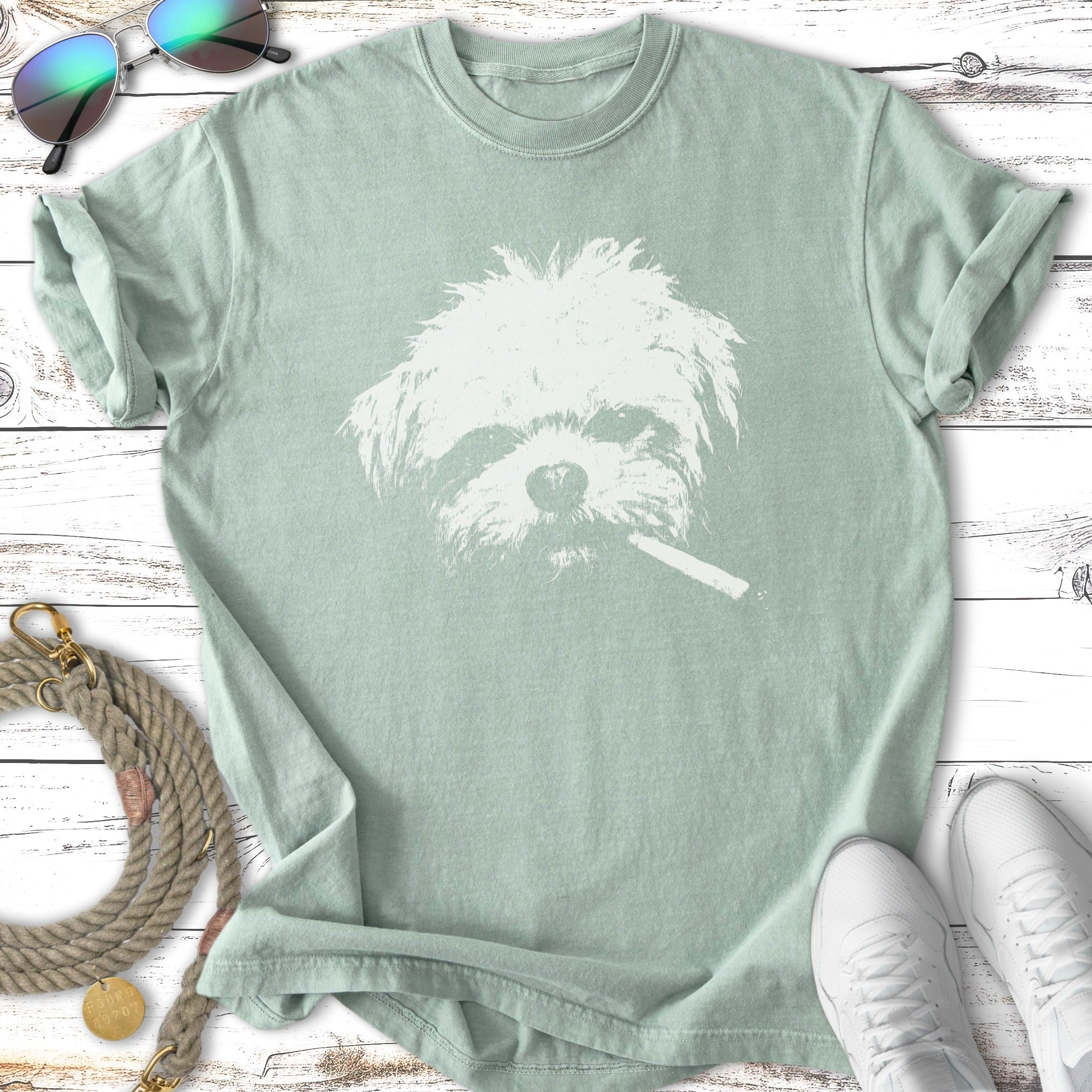 White dog wearing sunglasses with cigarette in mouth graphic on green t-shirt.