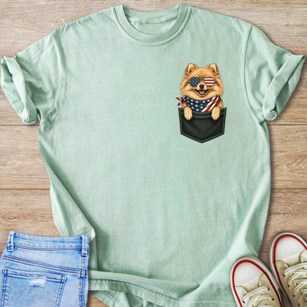 Pomeranian dog in pocket wearing American flag sunglasses and bandana on teal t-shirt.