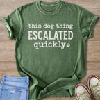 Green t-shirt with "this dog thing ESCALATED quickly" and paw print graphic.