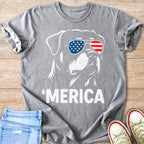 Dog wearing American flag sunglasses with "MERICA" text on t-shirt.