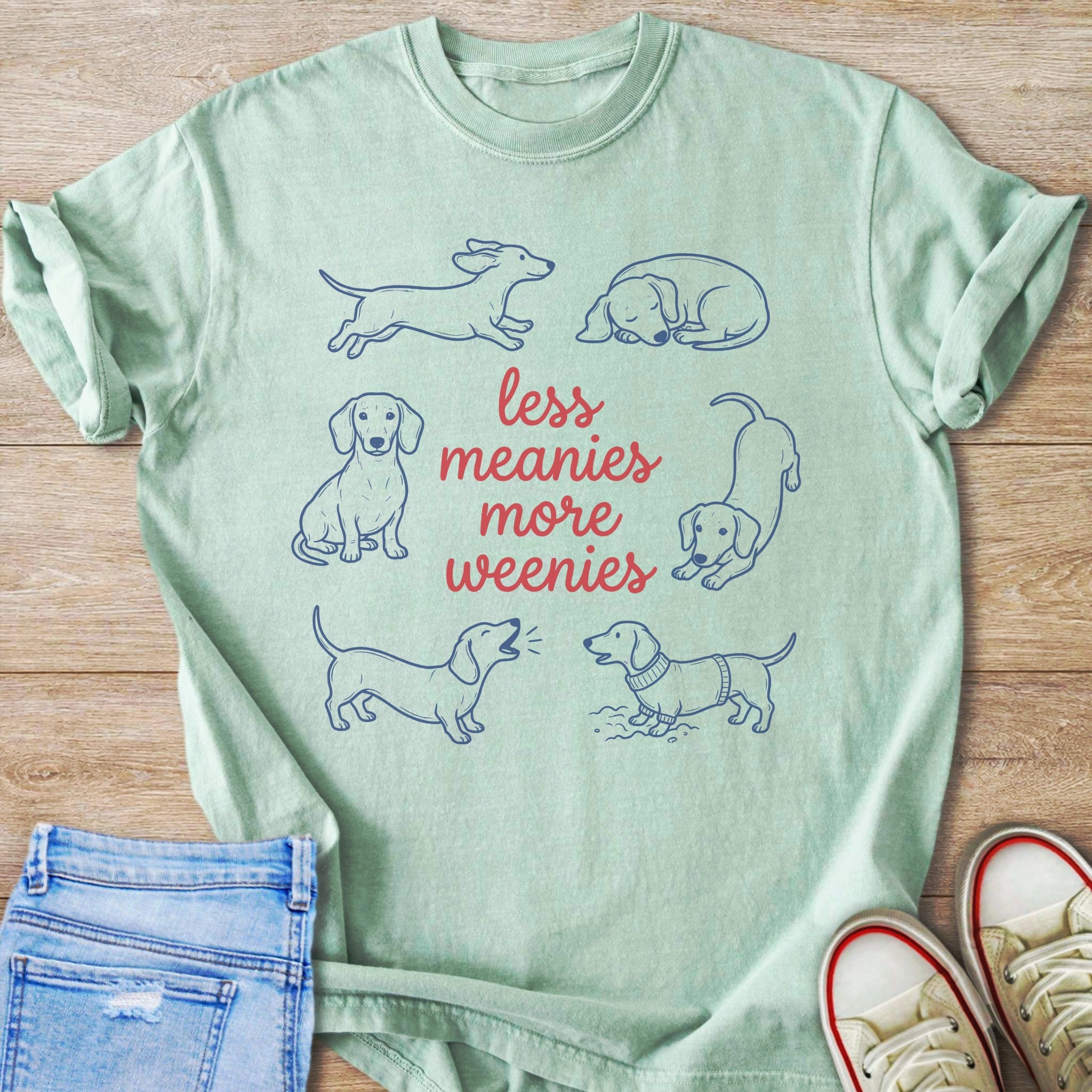 Mint green t-shirt with blue dachshund illustrations and text: "less meanies more weenies."