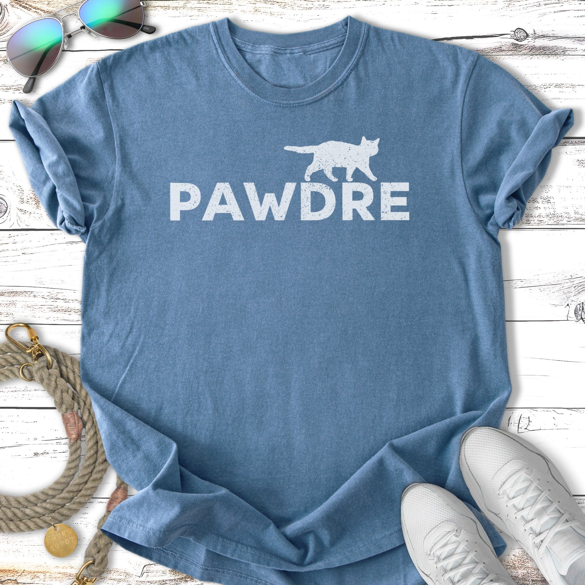 Blue t-shirt with white "PAWDRE" text, sunglasses, leash, and sneakers.