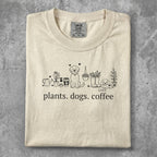 Cream t-shirt with line art of plants, dogs, and coffee cup, text reads "plants. dogs. coffee."