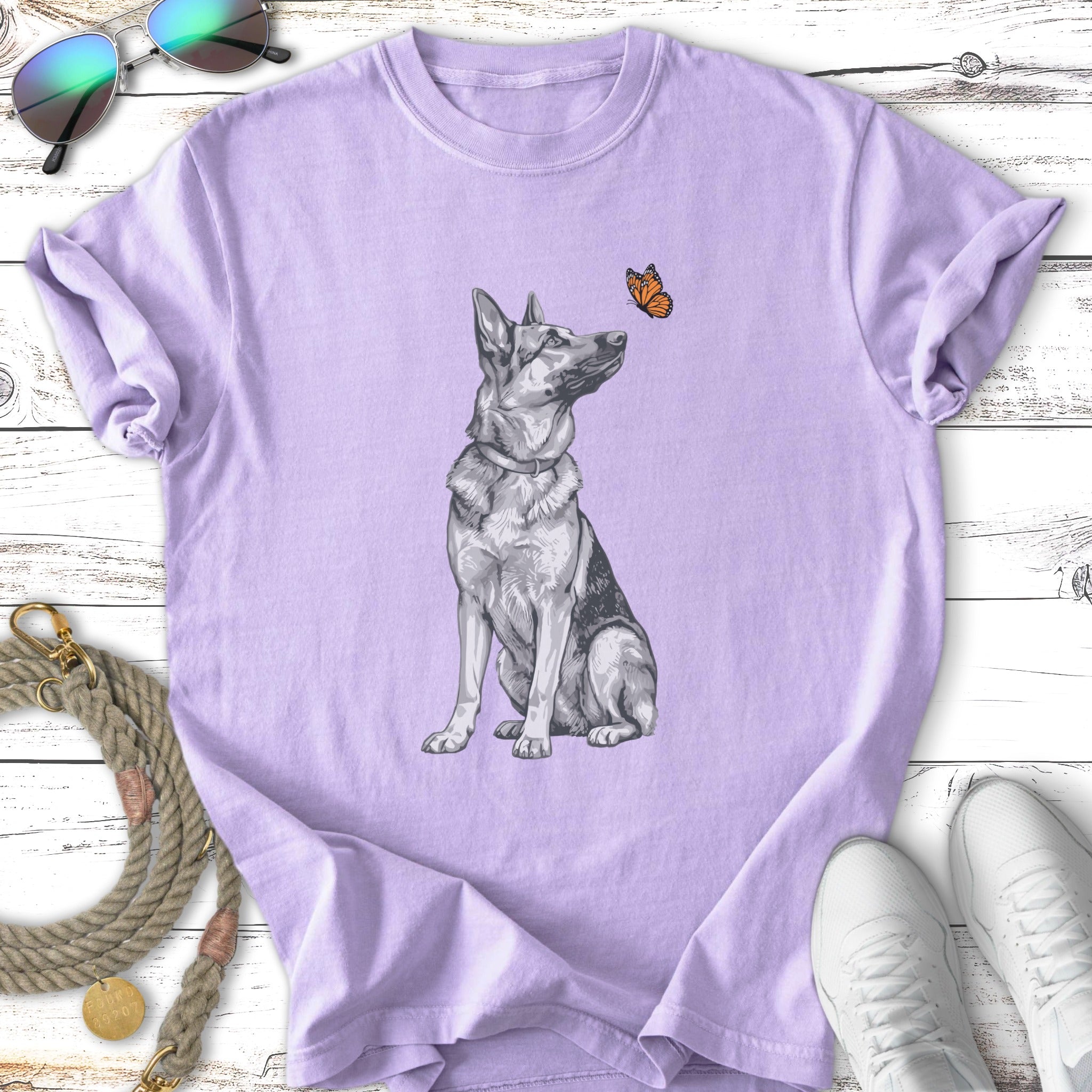 German Shepherd dog sits, looking up at a butterfly on a purple t-shirt.