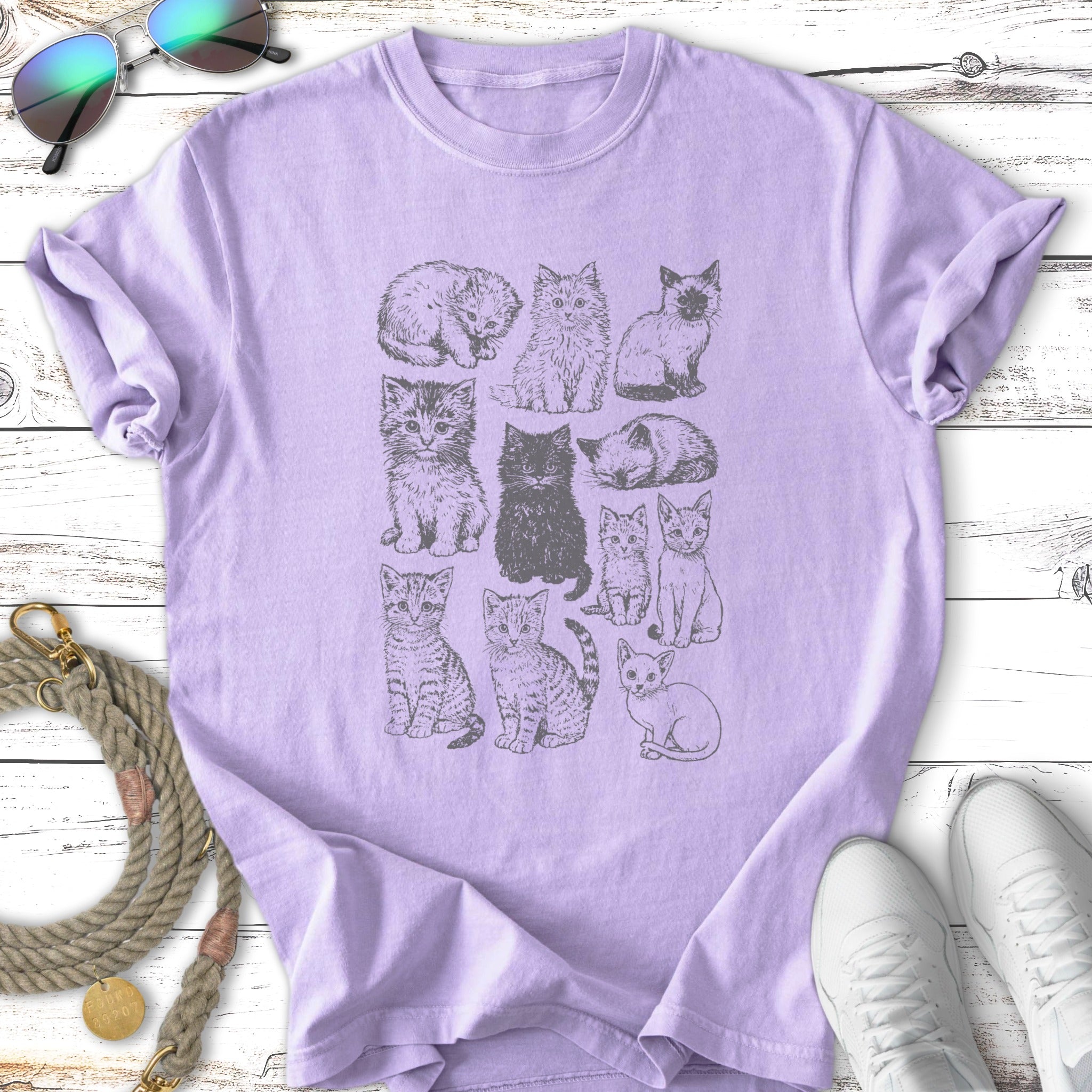 Line drawing of twelve kittens arranged in a grid on a lavender t-shirt.