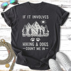 T-shirt with mountains, trees, sun, and paw prints. Text reads "If it involves hiking & dogs - count me in".