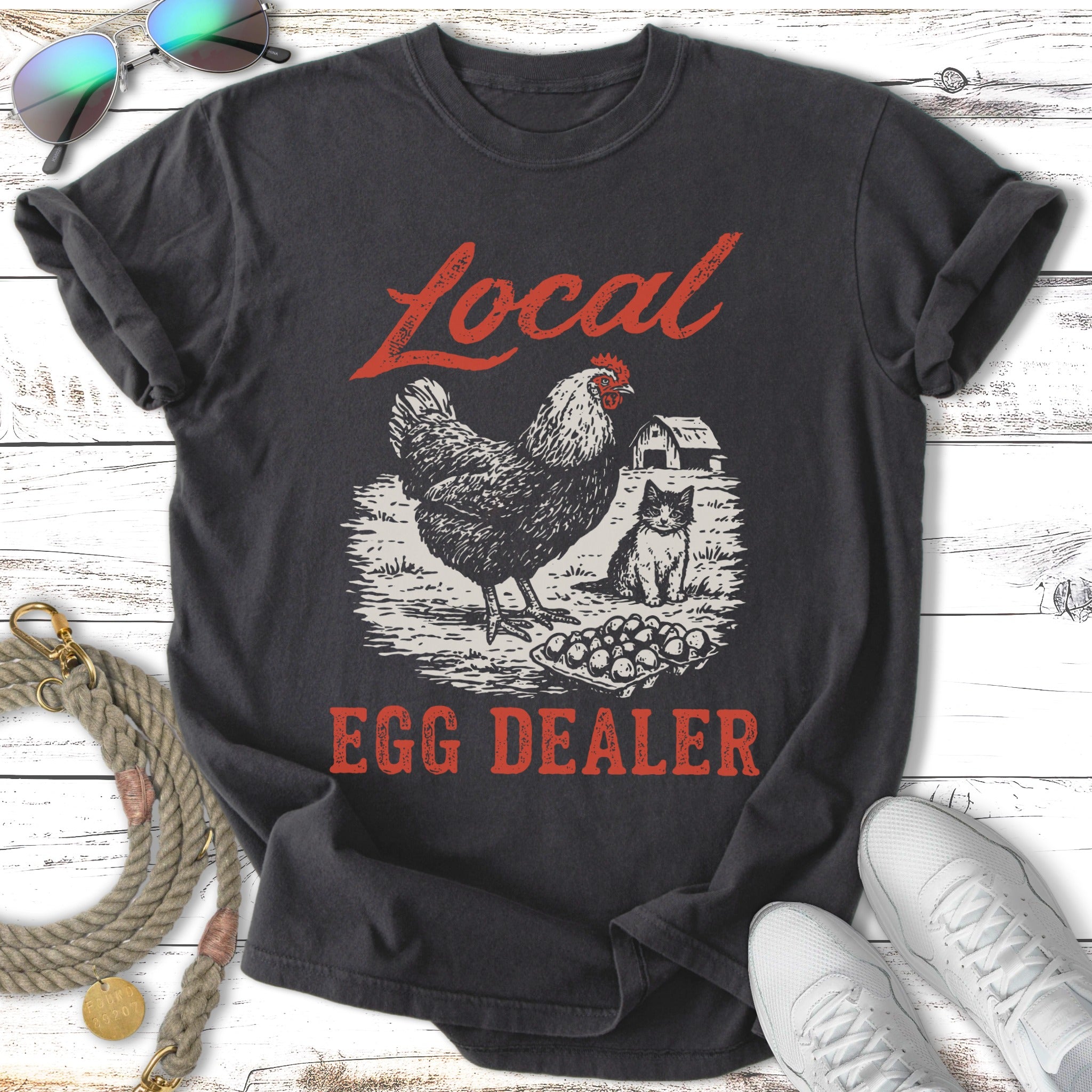 Dark t-shirt with "Local Egg Dealer" graphic of a chicken, cat, and eggs.