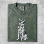 German Shepherd sitting and looking up at a small orange butterfly.