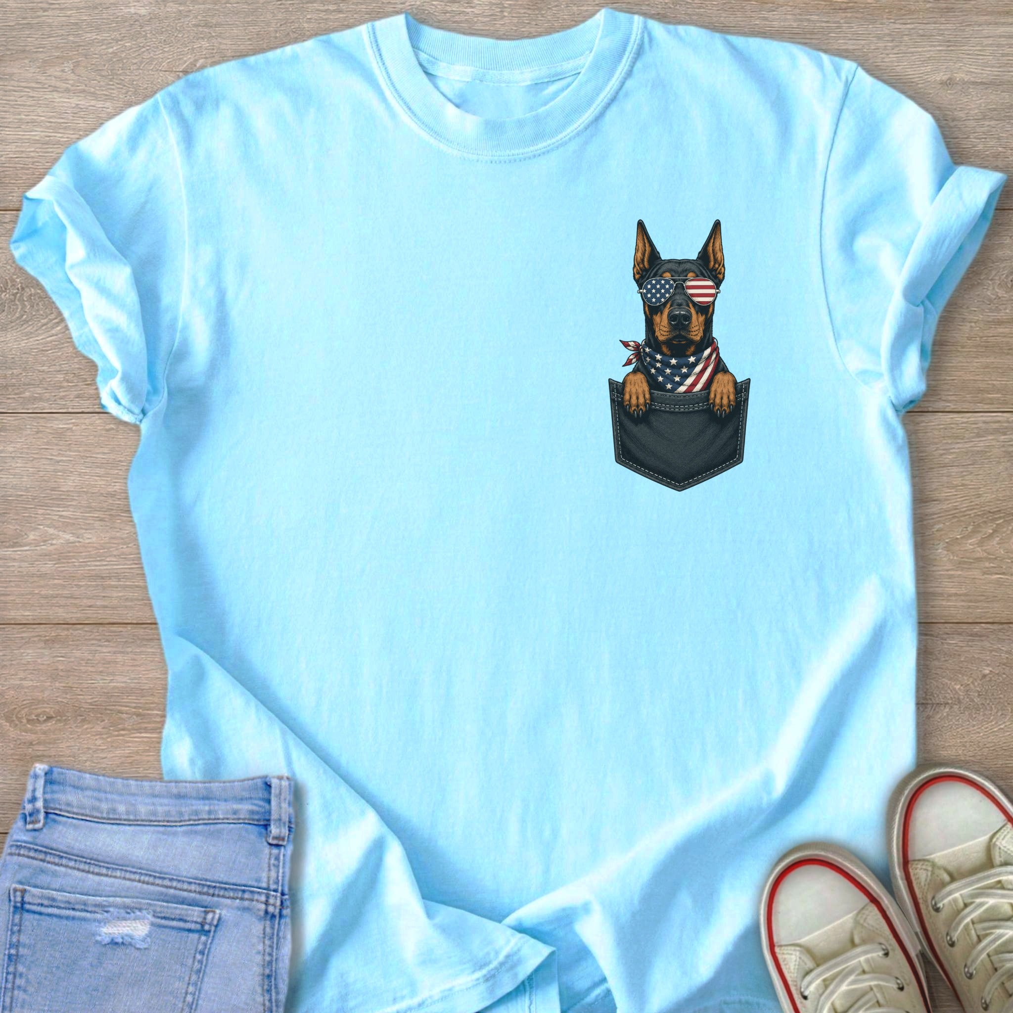 Light blue t-shirt with a Doberman wearing American flag sunglasses and bandana in a pocket.
