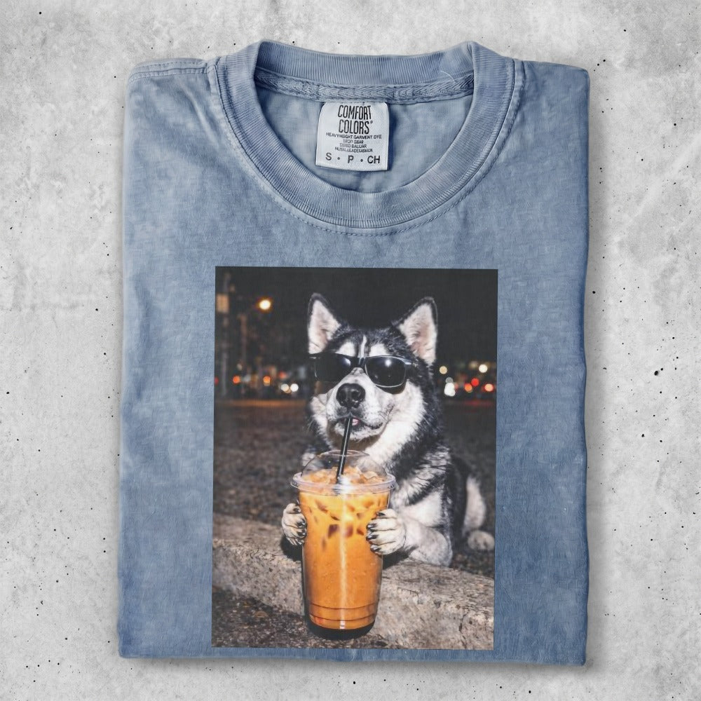 Husky dog wearing sunglasses holds iced coffee with blurred city lights background.