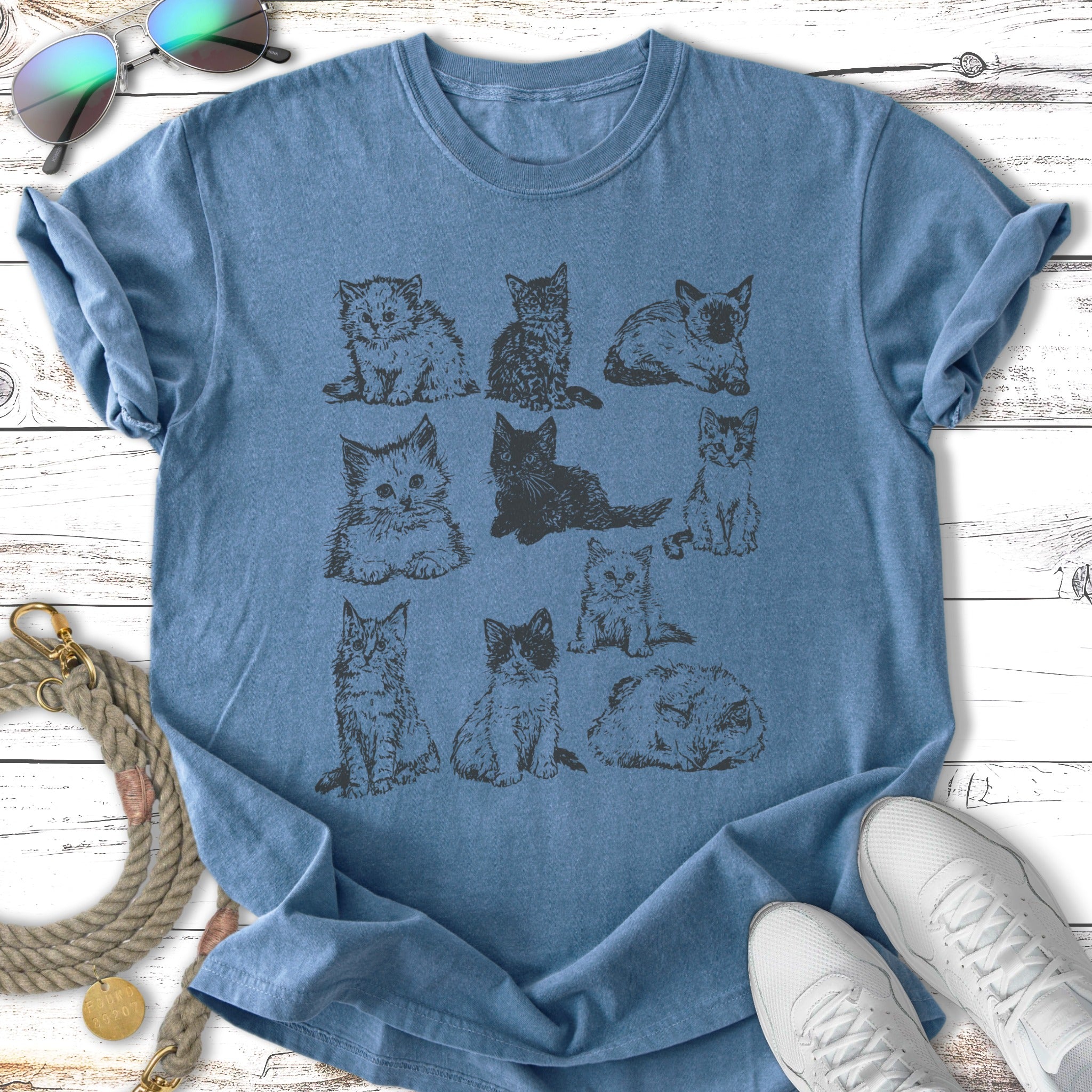 Line drawing of nine playful kittens on a blue t-shirt.