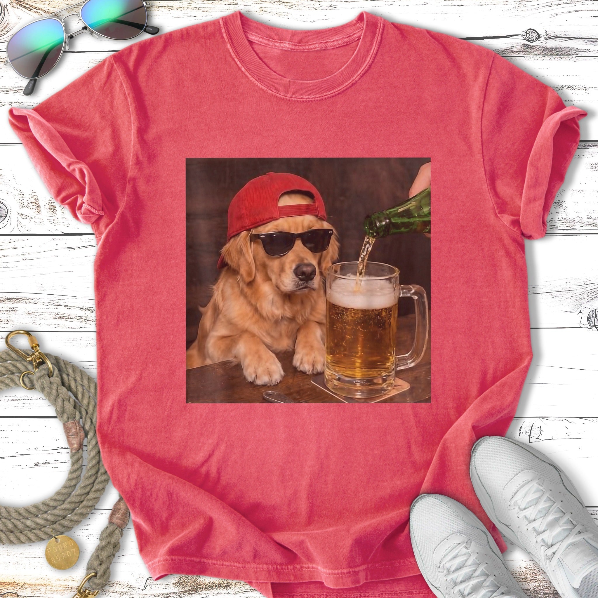 Golden retriever wearing a red baseball cap and sunglasses drinks beer.