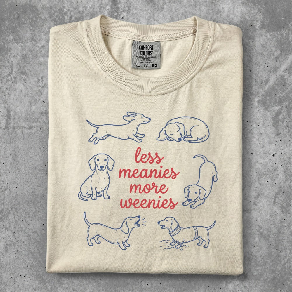 Cream t-shirt with blue dachshund illustrations and "less meanies more weenies" text.