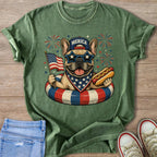 French bulldog in sunglasses holds American flag and hot dog in patriotic swim ring.