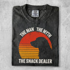 Black t-shirt with orange sunburst and dog silhouette, text "The Man The Myth The Snack Dealer".