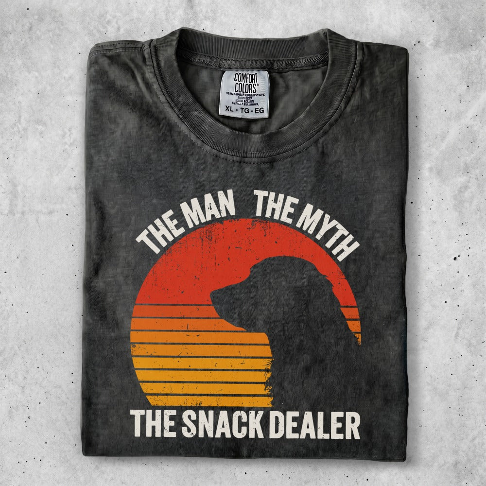 Black t-shirt with orange sunburst and dog silhouette, text "The Man The Myth The Snack Dealer".