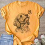 Gold t-shirt with line drawing of dog looking at butterfly.