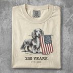Dachshund holding American flag, "250 Years 1776-2026" text, cream t-shirt.