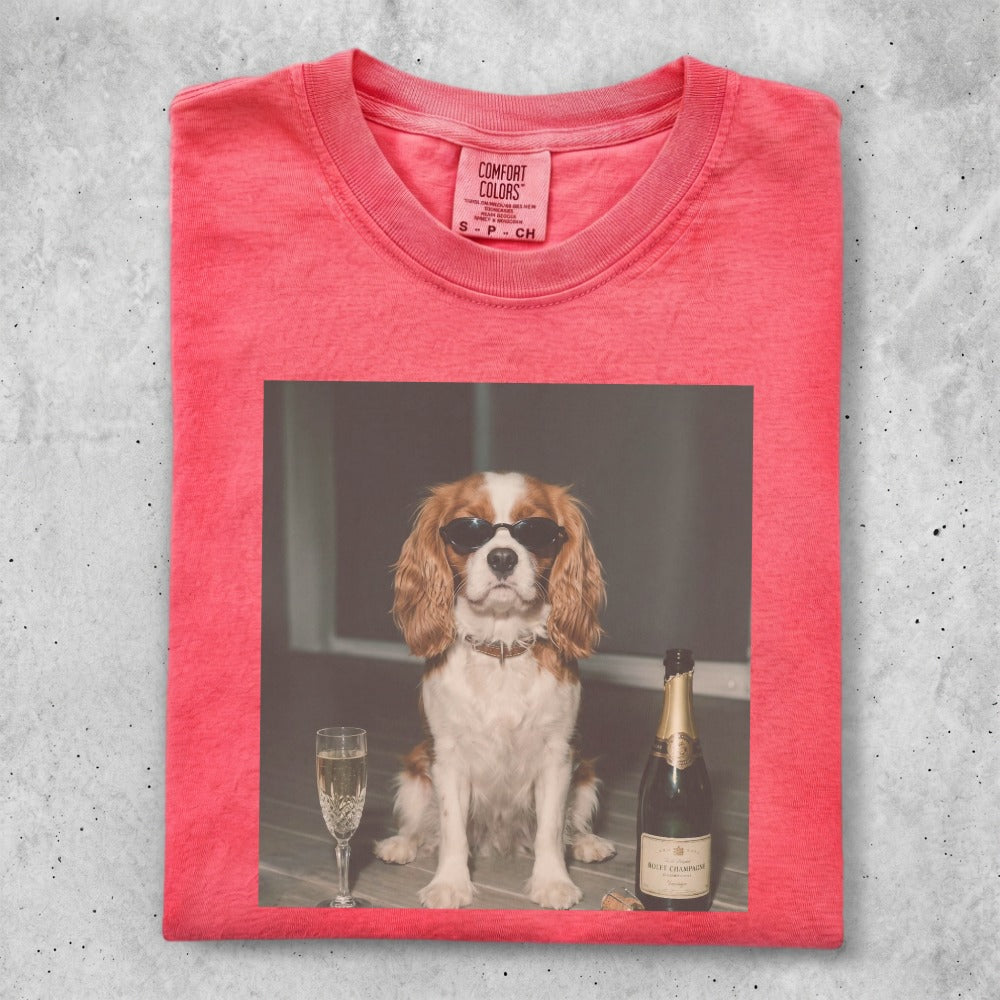 Dog in sunglasses sits next to champagne bottle and glass.