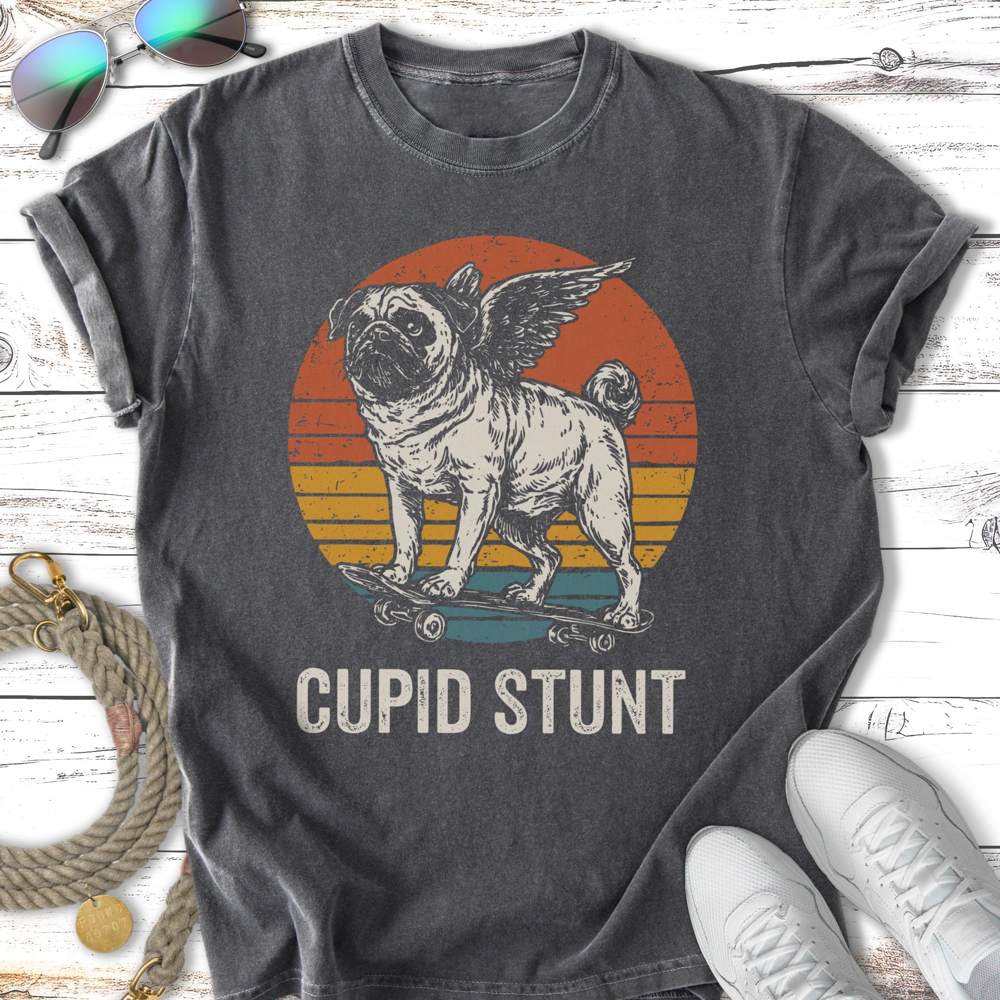 Pug with wings riding a skateboard, vintage sunset graphic, "Cupid Stunt" text.