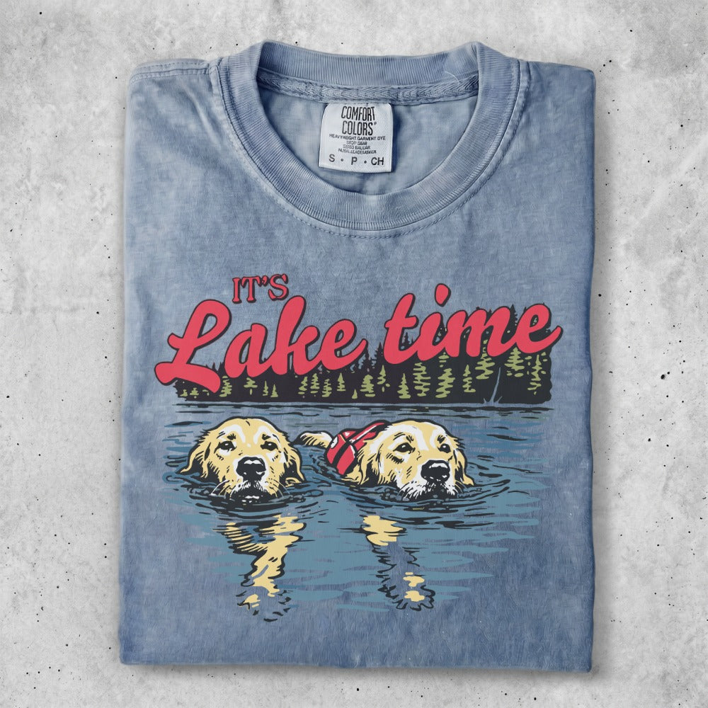 Two golden retrievers wearing life vests swim in a lake, "It's Lake time" text above.