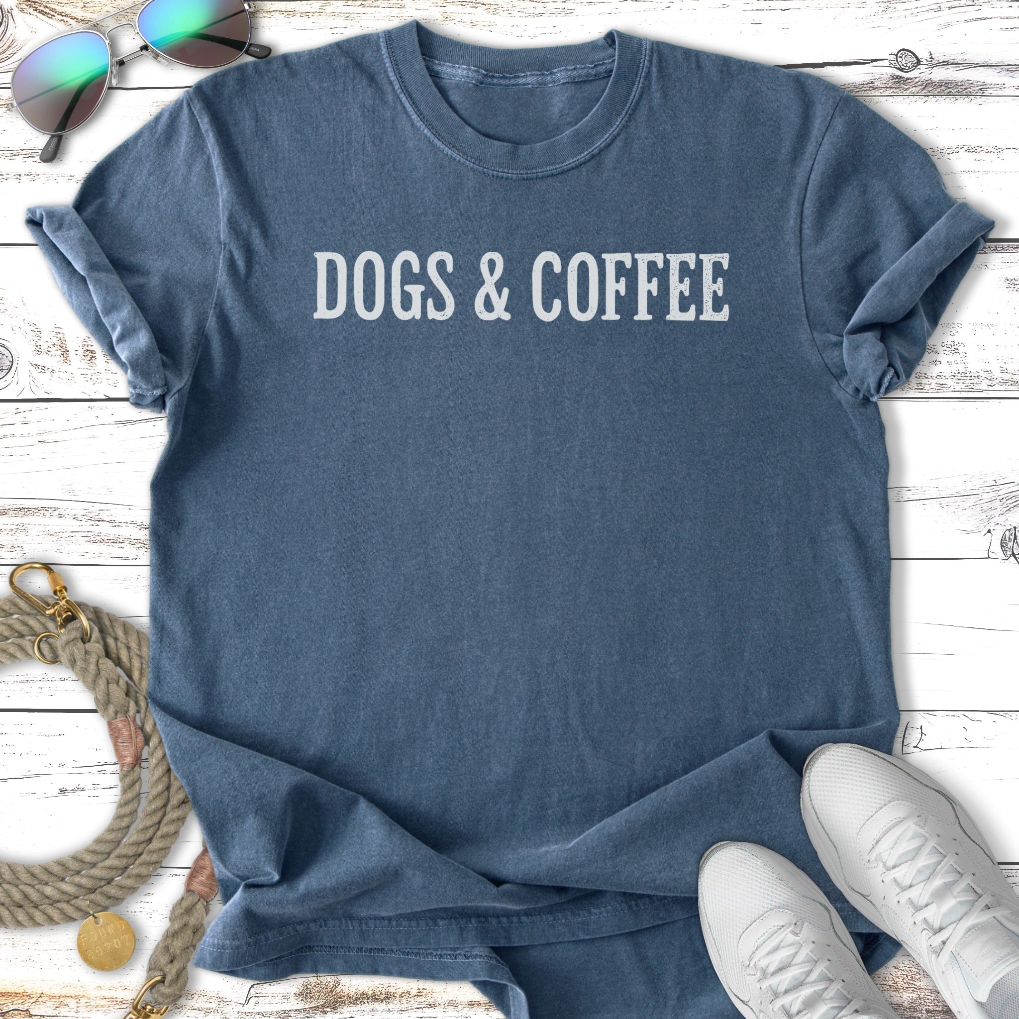 Blue t-shirt with "Dogs & Coffee" text, worn casually with sunglasses and sneakers.
