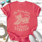 Coral t-shirt with a cartoon cat stretching and text "My Pussy Loves. A Good Stretch."